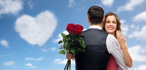 爱情,情侣,求婚情人节快乐的女人与订婚戒指玫瑰拥抱男人蓝天心形云背景女人带着订婚戒指玫瑰拥抱男人图片