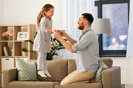 家庭,童父亲的快乐的父亲小女儿跳沙发上,家里玩得开心父亲女儿家里蹦蹦跳跳,玩得很开心图片