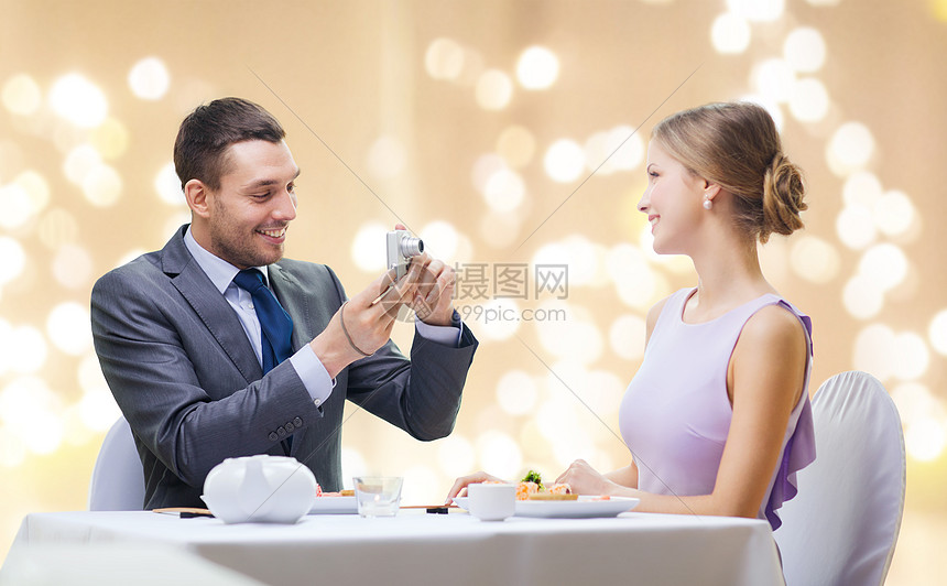 ‘~情侣技术休闲微笑的男人餐厅用数码相机米色背景上的节日灯上拍摄妻子女朋友的照片男人餐馆用照相机给表妹拍照  ~’ 的图片