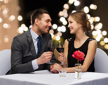约会,庆祝情人节的微笑的轻夫妇碰杯含酒精的红酒,并节日灯光的背景上互相看着轻的夫妇餐厅喝了杯酒图片