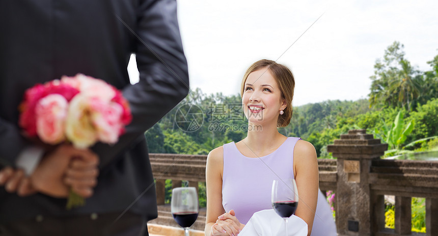 情侣,约会情人节微笑的轻女人看着男人背后的花餐厅的夏天背景女人看着餐厅里花的男人图片