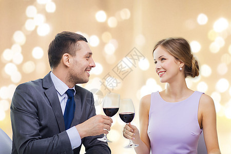 约会庆祝情人节的微笑的轻夫妇碰杯含酒精的红酒,并米色背景上的节日灯上看着其他餐厅轻的夫妇餐厅喝了杯图片