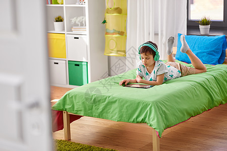 童,技术人的男孩与平板电脑耳机躺床上家家里平板电脑耳机的男孩图片