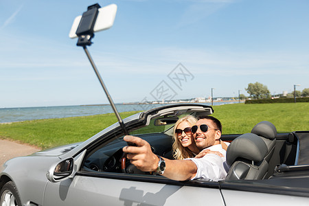 公路旅行,休闲,技术人的快乐夫妇敞篷汽车拍摄智能手机自拍杆幸福的夫妇汽车上用智能手机自拍图片