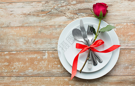情人节,餐桌浪漫的晚餐套盘子餐具系红色丝带与玫瑰花木背景顶部套盘子上的红玫瑰花图片