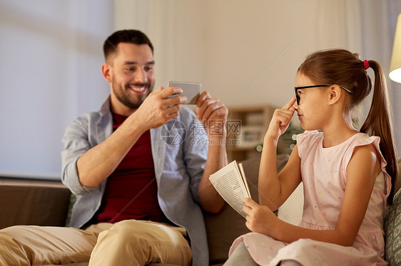 家庭技术人的快乐的父亲晚上家用智能手机拍摄女儿父亲家用手机给女儿拍照图片