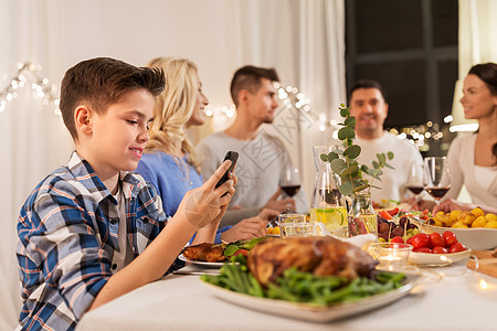 技术,假期人的快乐的男孩与智能手机家里举行家庭晚宴带智能手机的男孩家庭晚宴上图片