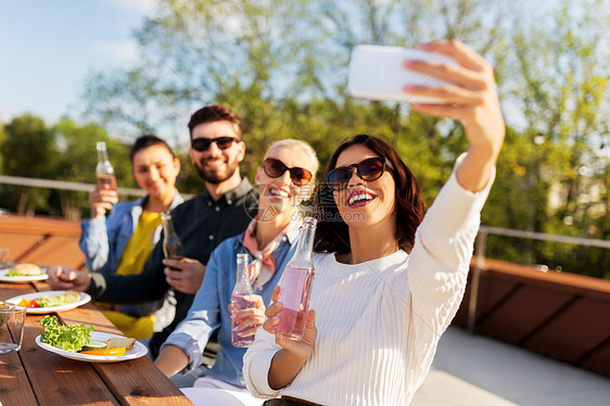 休闲人们的快乐的朋友与饮料屋顶上举行晚餐聚会,智能手机自拍快乐的朋友屋顶派上自拍图片