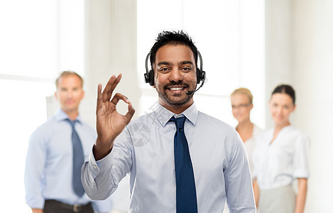商业,客户服务人的微笑的印度商人帮助热线运营商耳机同事的背景上OK手势商人帮助热线接线员OK标志图片