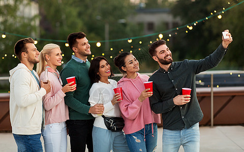 休闲人们的快乐的朋友聚会杯里喝饮料,夏天用智能手机屋顶上自拍饮料的朋友屋顶派上自拍图片