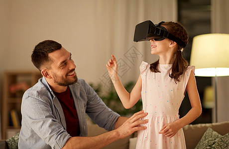 家庭,虚拟现实娱乐活动快乐的父亲小女儿戴着VR眼镜,晚上家玩电子游戏父亲女儿戴着VR眼镜家玩背景