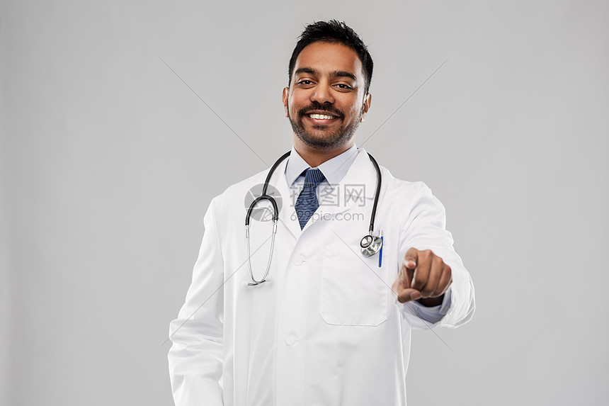 医学,职业医疗微笑的印度男医生穿着白色外套,听诊器指着你灰色背景微笑的印度男医生指着你图片