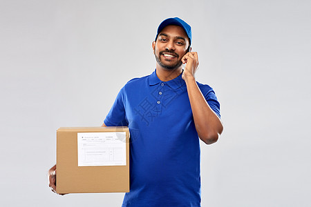 邮件服务,沟通装运快乐的印度送货人与智能手机包裹箱蓝色制服灰色背景带智能手机包裹箱的印度送货员图片