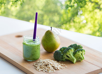 婴儿食品,健康饮食营养璃罐与绿色素泥木制切割板自然背景木板上果泥婴儿食品的罐子图片