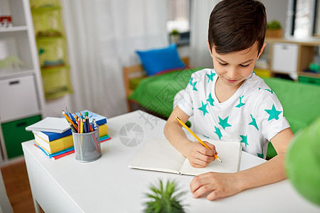 教育,童学校的快乐的小男孩坐桌子上,家用铅笔写字画画笔记本上快乐的男孩家里写字画画笔记本上图片