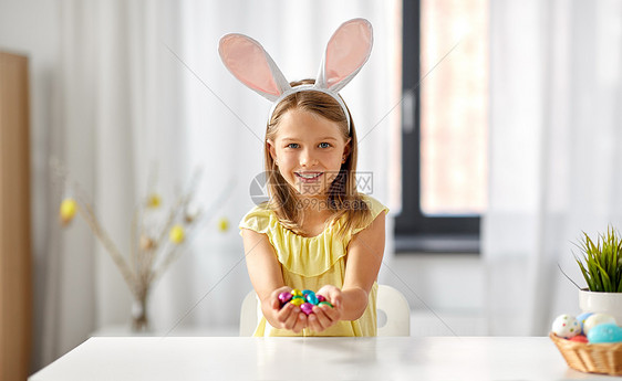 复活节,假日人们的快乐的女孩戴着兔子耳朵,头带着巧克力蛋家家里巧克力复活节彩蛋的快乐女孩图片