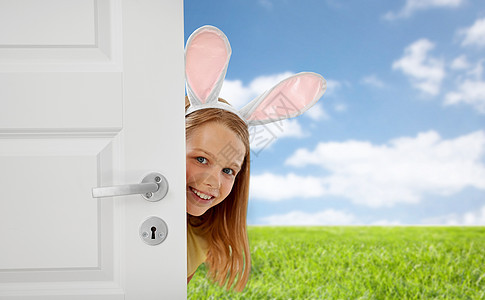 复活节,假日人们的快乐的女孩戴着兔子的耳朵,蓝天草地背景上窥视着门外快乐的女孩,复活节兔子的耳朵偷看门外背景图片