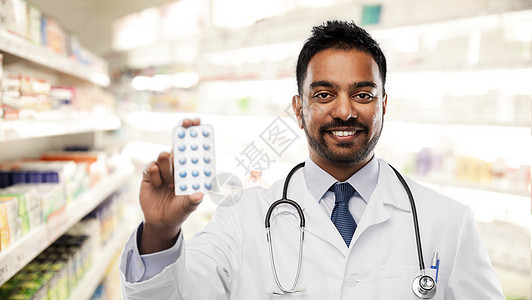 医药,药房医疗保健微笑的印度男医生药剂师穿着白色外套,药店背景下服用药丸带药丸的印度男医生药剂师图片