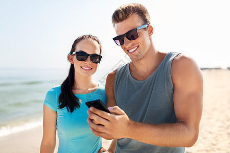 健身,运动生活方式的快乐的夫妇穿着运动服装太阳镜,海滩上智能手机穿着运动服智能手机的夫妇海滩上图片