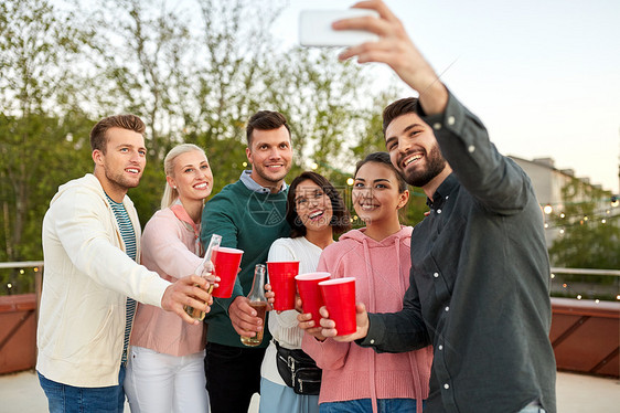 休闲人们的快乐的朋友与非酒精饮料自拍智能手机屋顶聚会夏季饮料的朋友屋顶派上自拍图片