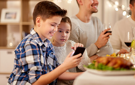 技术,假期人的快乐的男孩妹妹用智能手机家里举行家庭晚宴带妹妹的男孩家庭晚餐时用智能手机图片