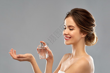 香水,美丽奢侈的快乐的微笑轻女子喷洒香水她的手腕灰色的背景带着灰色背景的香水的快乐女人图片