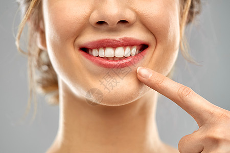 口腔护理,牙科卫生人们的近距离手指指向女的脸,健康的白牙灰色背景靠近女人指着她洁白的牙齿背景图片