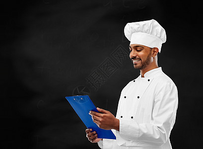 烹饪,职业人的快乐的男印度厨师托克与剪贴板黑色黑板背景厨师黑板上阅读黑板上的菜单图片