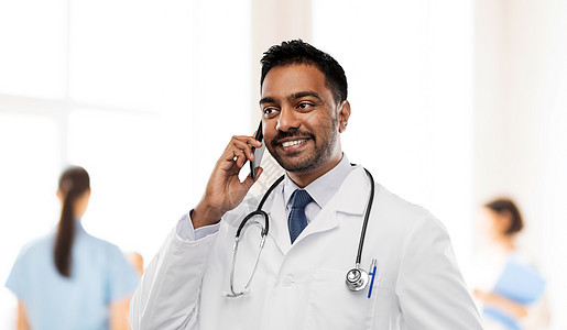 医学,技术医疗保健微笑的印度男医生穿着白色外套,听诊器医院背景下拨打智能手机微笑的印度男医生打电话给智能手机图片