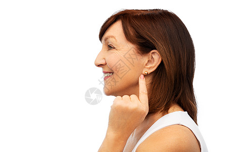 美丽老人的微笑的老年女子的轮廓指向她的金色耳环超过白色微笑的高级女人指着她的耳环图片