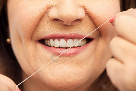 牙齿护理卫生的人的近距离微笑的老年女子清洁她的牙齿用牙线白色的背景老妇女用牙线清洁牙齿图片