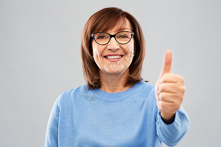 手势,视觉老人的微笑的老妇女眼镜上的肖像,灰色背景上竖大拇指老妇女的肖像竖大拇指图片