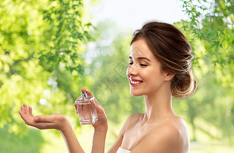 香水,美丽奢侈的快乐的微笑轻女子喷洒香水她的手腕上绿色的自然背景带着灰色背景的香水的快乐女人图片