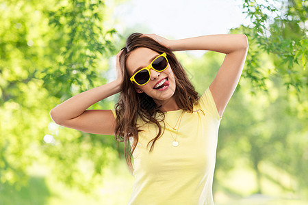 夏天,配饰人的微笑的轻女人十几岁的女孩穿着T恤太阳镜,绿色的自然背景下抱着她的头穿着黄色太阳镜t恤的图片