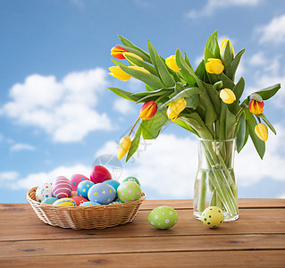 复活节,假日,传统物体篮子里的彩色鸡蛋桌子上的郁金香花,蓝天云彩背景篮子里的彩色复活节彩蛋天空上的花图片