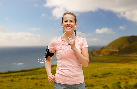 健身,运动健康的生活方式微笑的女人戴着智能手机,加州大海岸背景下跑步听音乐带着耳机的女人户外跑步图片