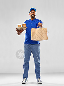 服务人的快乐的印度送货人,包里食物,灰色背景下穿着蓝色制服的饮料快乐的印度送货人带着食物饮料图片