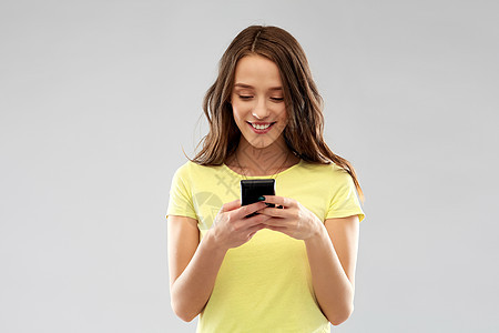 技术人的微笑的轻妇女十几岁的女孩穿着空白的黄色T恤,用智能手机灰色背景用智能手机的轻女少女图片