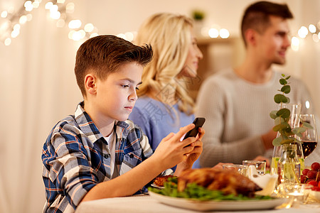 家庭晚餐技术,假期人的快乐的男孩与智能手机家里举行家庭晚宴带智能手机的男孩家庭晚宴上背景