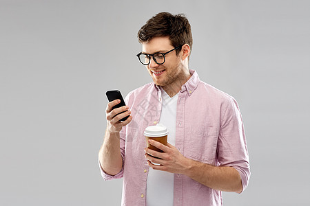 外卖人们的轻人学生戴着智能手机喝咖啡的灰色背景戴眼镜的男人着智能手机喝咖啡图片