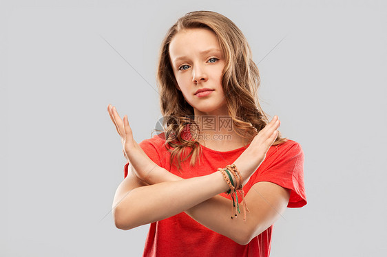禁止人的严肃的少女灰色背景上表现出交叉的手禁止的手势十几岁的女孩用令人讨厌的手势交叉双手图片