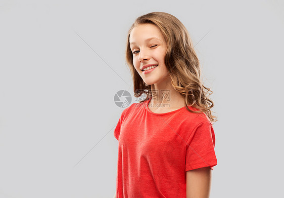 人们的微笑的十几岁女孩,长发红色的t恤上闪烁着灰色的背景微笑的十几岁女孩穿着红色T恤眨眼图片