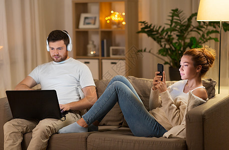 休闲,技术人的快乐的夫妇与笔记本电脑,耳机智能手机听音乐家里晚上夫妇带着笔记本电脑智能手机家休息图片