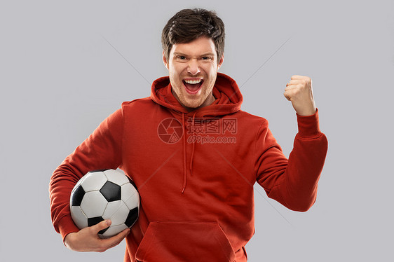 运动,休闲游戏获胜快乐的人足球迷穿着红色帽衫,带着足球庆祝胜利,并灰色背景上拳泵手势快乐的人足球迷,足球获胜图片