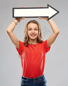 方向人们的微笑的十几岁女孩,长发红色的t恤上,着白色的大箭头,右边灰色的背景微笑的十几岁女孩用箭头方向图片