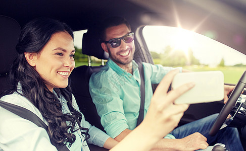 公路旅行,休闲,夫妇,技术人的快乐的男人女人开车自拍与智能手机幸福的夫妇汽车上自拍与智能手机图片