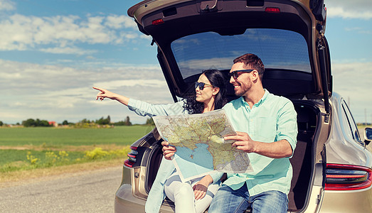 休闲,公路旅行,旅行人们的快乐的男人女人上搜索位置,坐户外的掀背车后备箱上幸福的男人女人掀背车的路线图图片