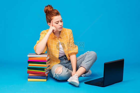 教育,高中,技术人的悲伤的红头发十几岁的学生女孩穿着格子衬衫撕裂的牛仔裤与书籍用笔记本电脑明亮的蓝色背景悲伤的图片