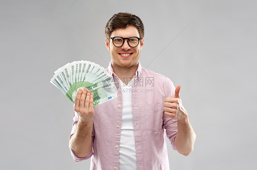 ‘~金钱,金融,商业人的快乐的轻人戴着眼镜,百欧元的钞票,灰色背景下竖大拇指快乐的轻人用欧元的钱竖大拇指  ~’ 的图片