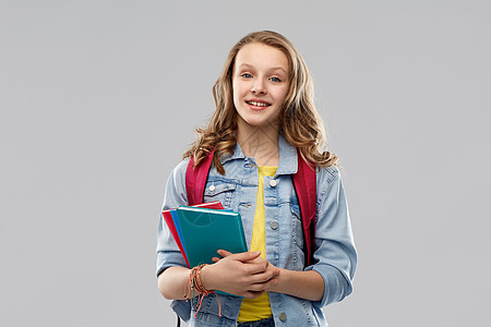教育,学校人的快乐微笑的十几岁的学生女孩带着灰色背景的书包书带着书包的快乐微笑的十几岁的学生女孩背景图片